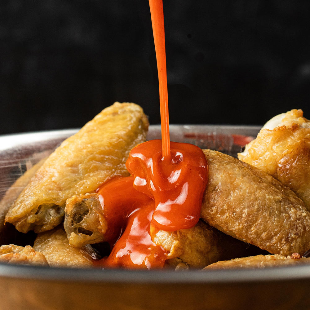 Frank's RedHot en cocina profesional con varias botellas, pensado para alto consumo