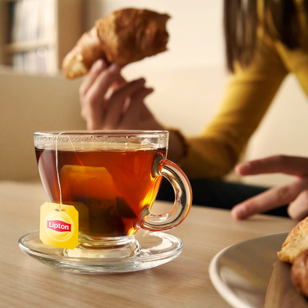 Manos vertiendo té Lipton en vaso, preparación rápida en casa u oficina